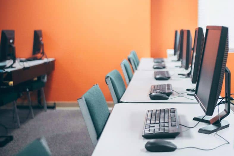 Laptops and monitors arranged on a long table in a computer lab or training room