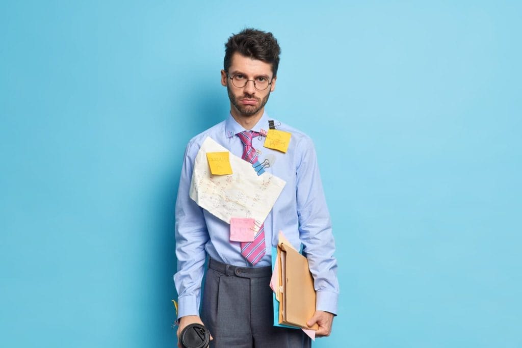 Overwhelmed business professional with sticky notes and documents cluttered on his shirt holding a coffee cup and folder expressing stress and chaos at work