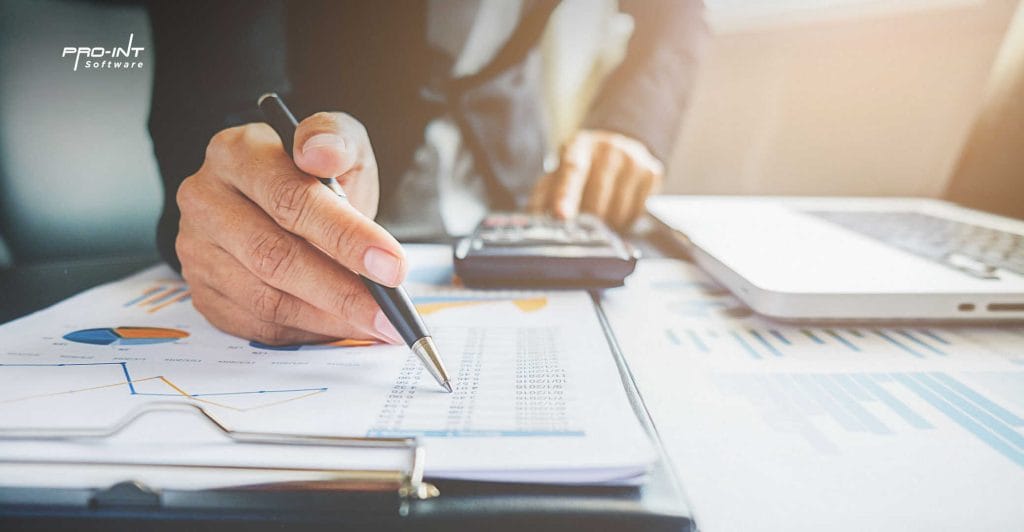 Hand analyzing financial data on printed charts and graphs with a pen laptop and calculator on a desk representing HRIS and ERP software solutions in Indonesia