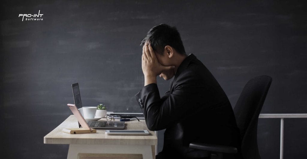 3bagian-implikasi - Pro-Int Software Man stressed over work or technical issues with HRIS ERP software on laptop sitting at a desk in an office representing software challenges or system overloads
