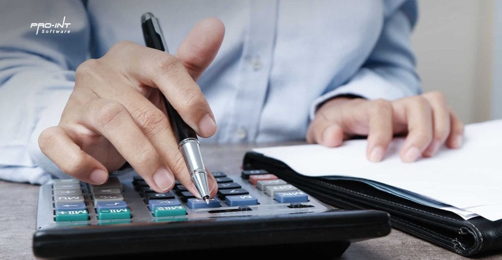High angle close up of a person using a calculator with a pen notebooks and documents on the desk emphasizing professional office work and financial management showcasing Pro Ints HRIS and ERP software solutions